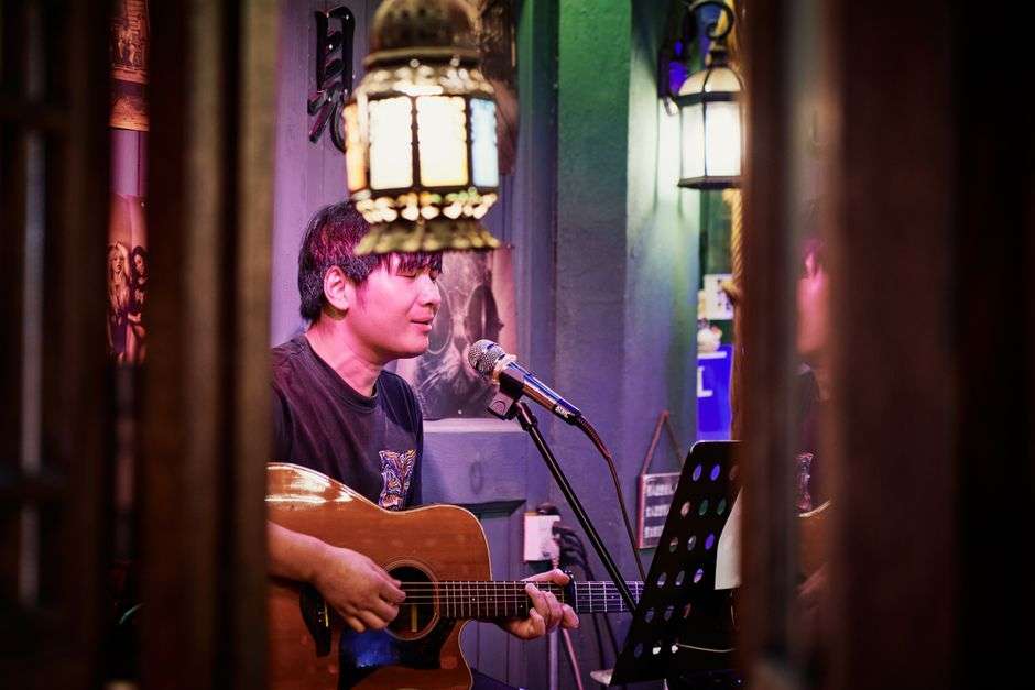 A musician plays acoustic guitar and sings at an intimate indoor listening room venue