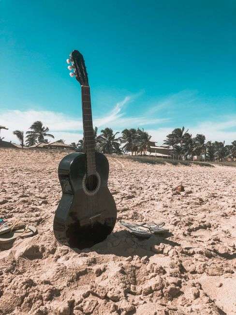 An acoustic guitar resting near a coastal, tropical setting evoking laid-back beach music