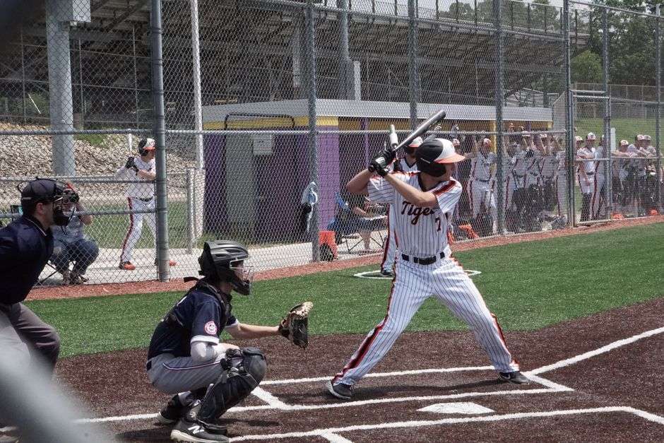 High school baseball players in action during a playoff game, with a batter at the plate and the catcher and umpire behind him