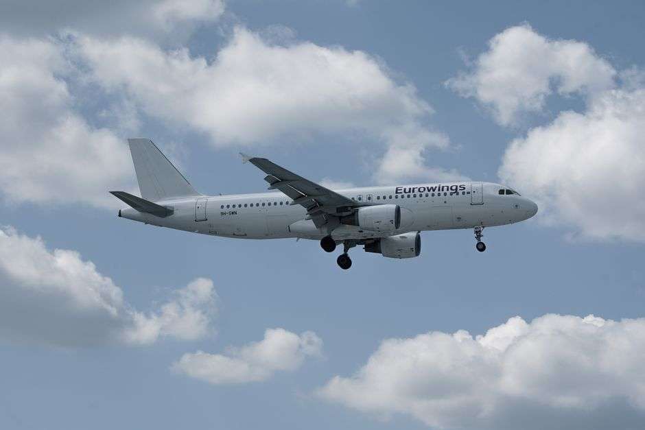 An Airbus A320 commercial jet flies against a partly cloudy sky