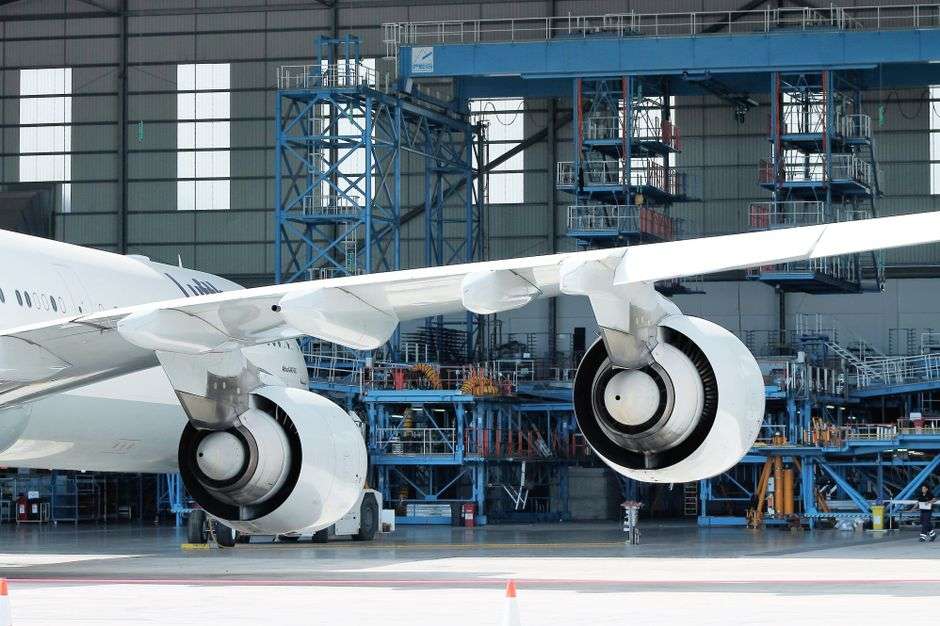 An aircraft engine and wing are seen up close inside an assembly hangar