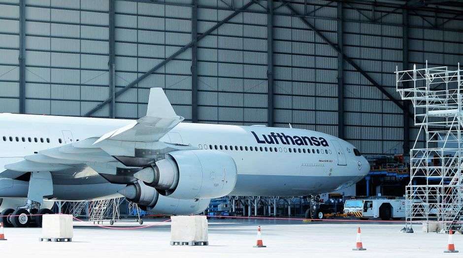 A commercial jet aircraft undergoes work inside a large assembly hangar