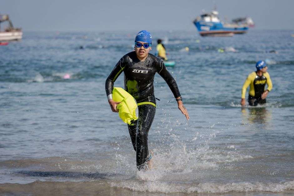 A triathlete in a wetsuit emerges from ocean water during the swim portion of a coastal triathlon