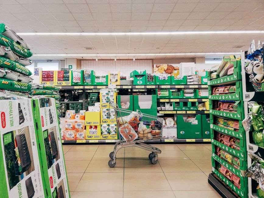 Shopping cart in a grocery store aisle stocked with products