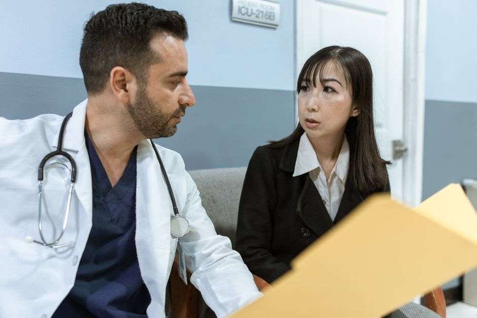 A physician in a white coat speaks with a hospital administrator in a hallway