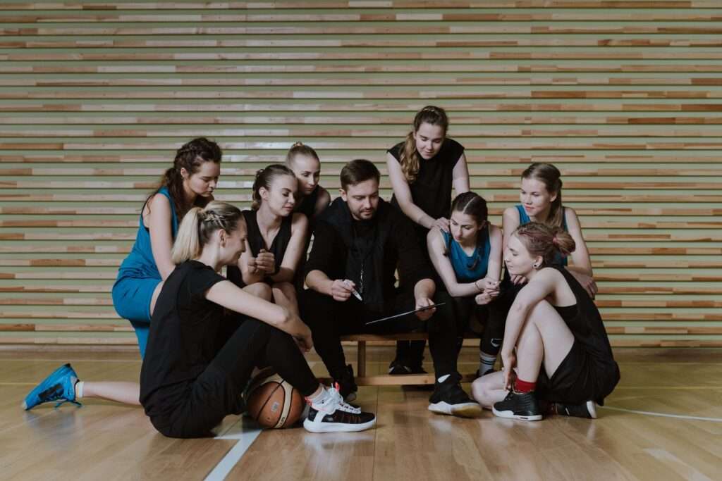 A basketball coach talks strategy with players during practice in a gymnasium