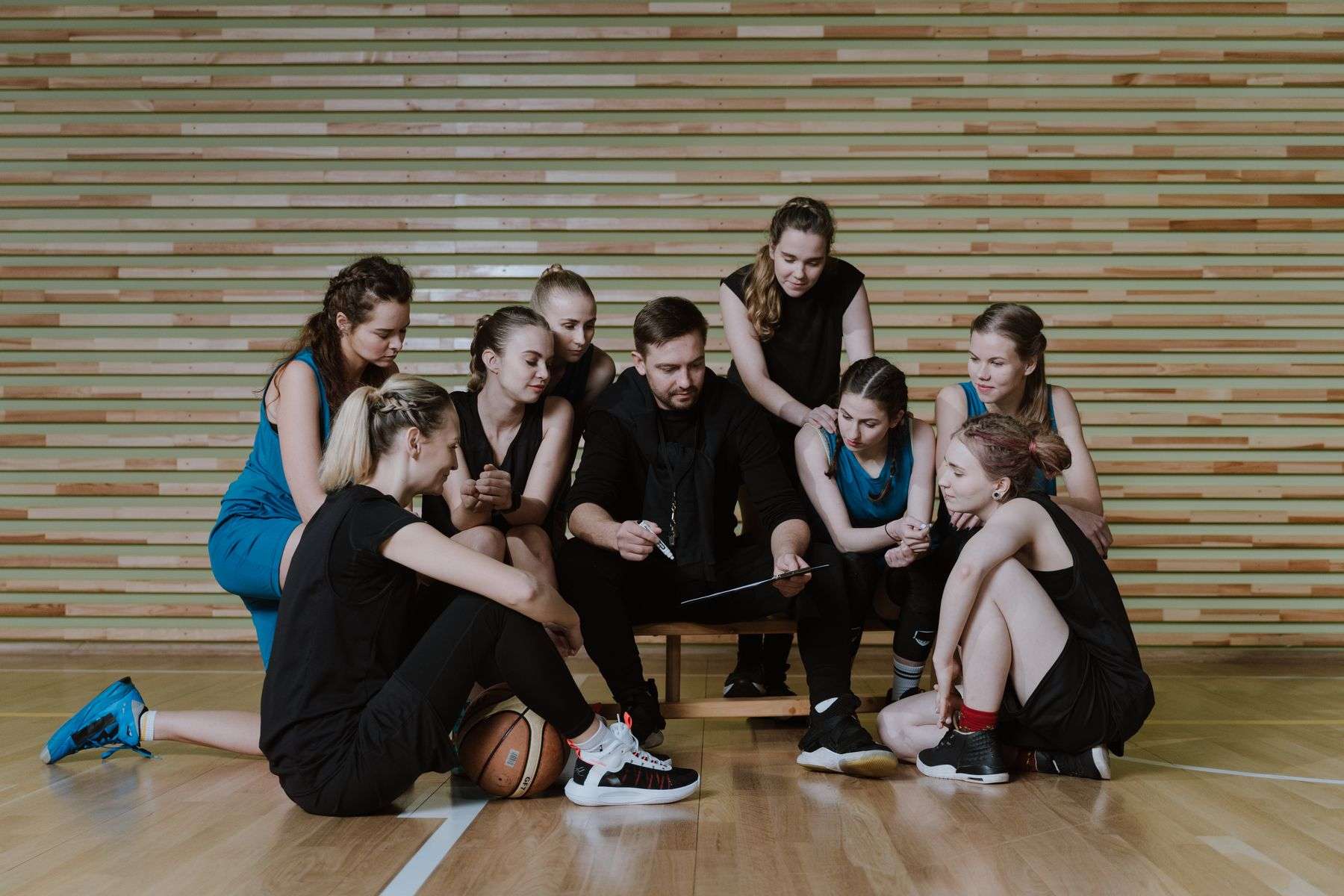A basketball coach talks strategy with players during practice in a gymnasium