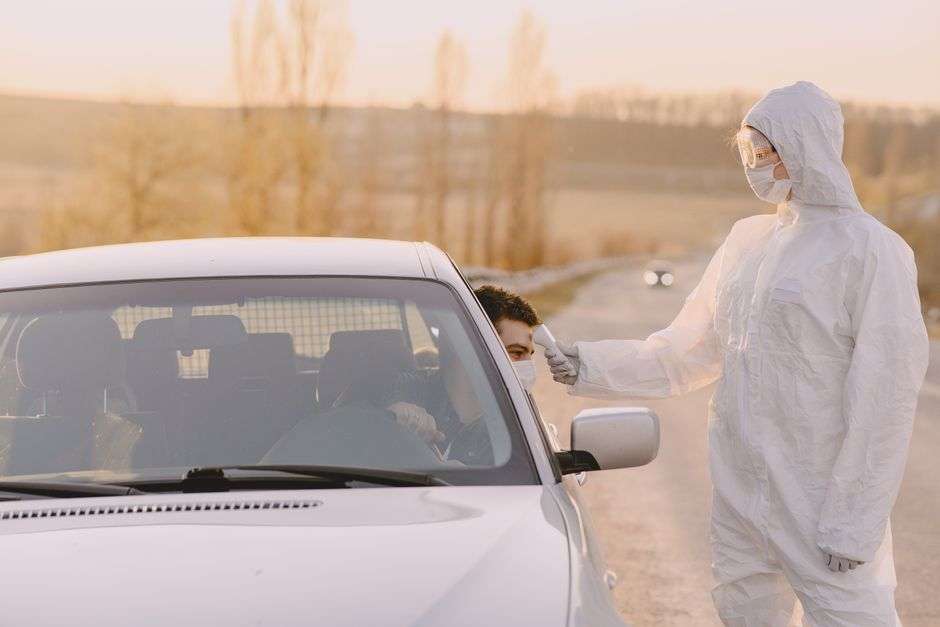A medical worker in protective gear checks a driver at a vehicle-based COVID-19 testing site