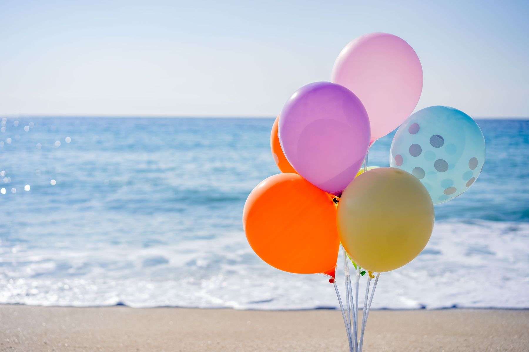 A bunch of colorful balloons floating near the ocean along a Gulf Coast beach