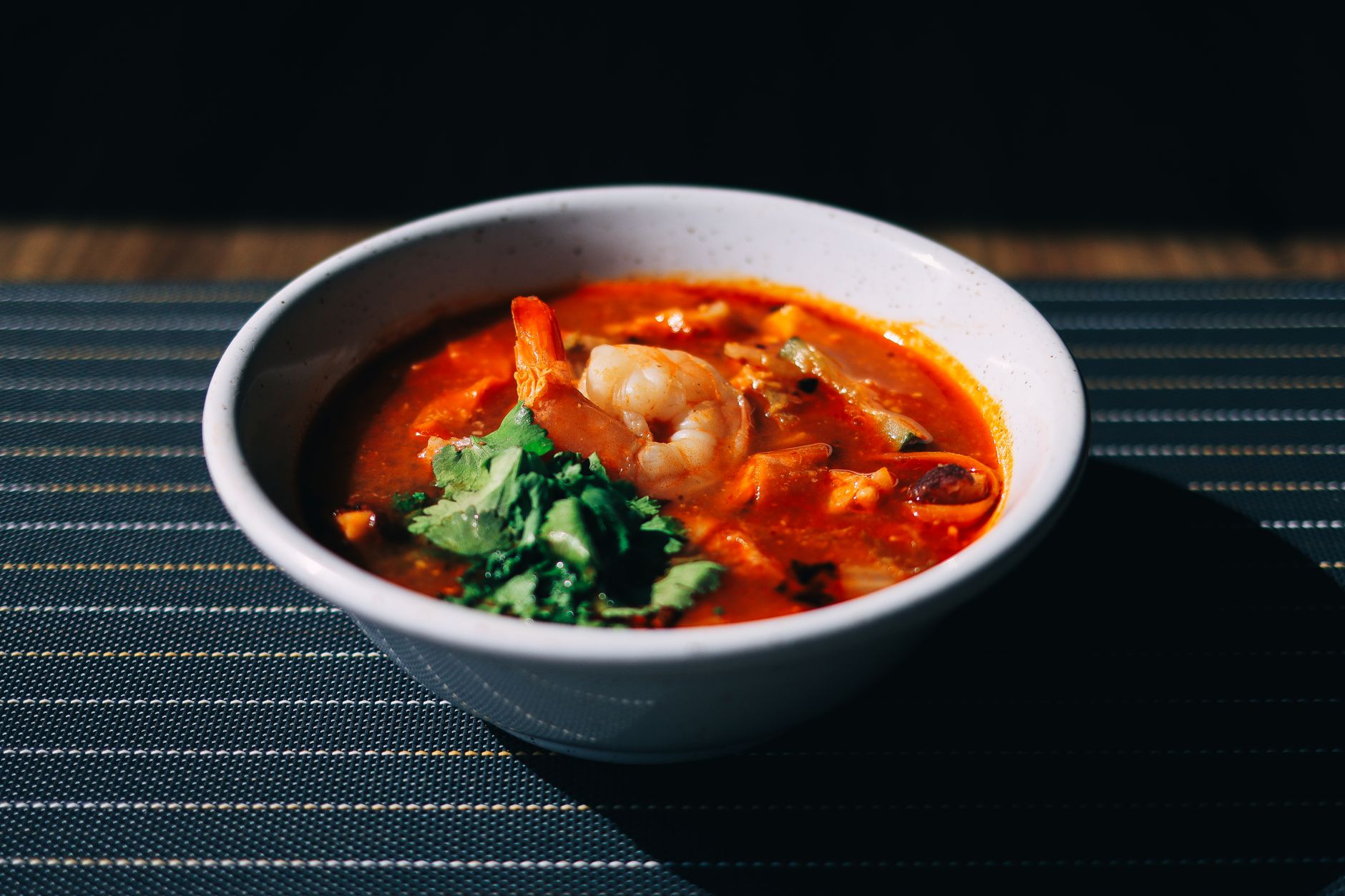 A dark bowl of seafood gumbo with crab claws