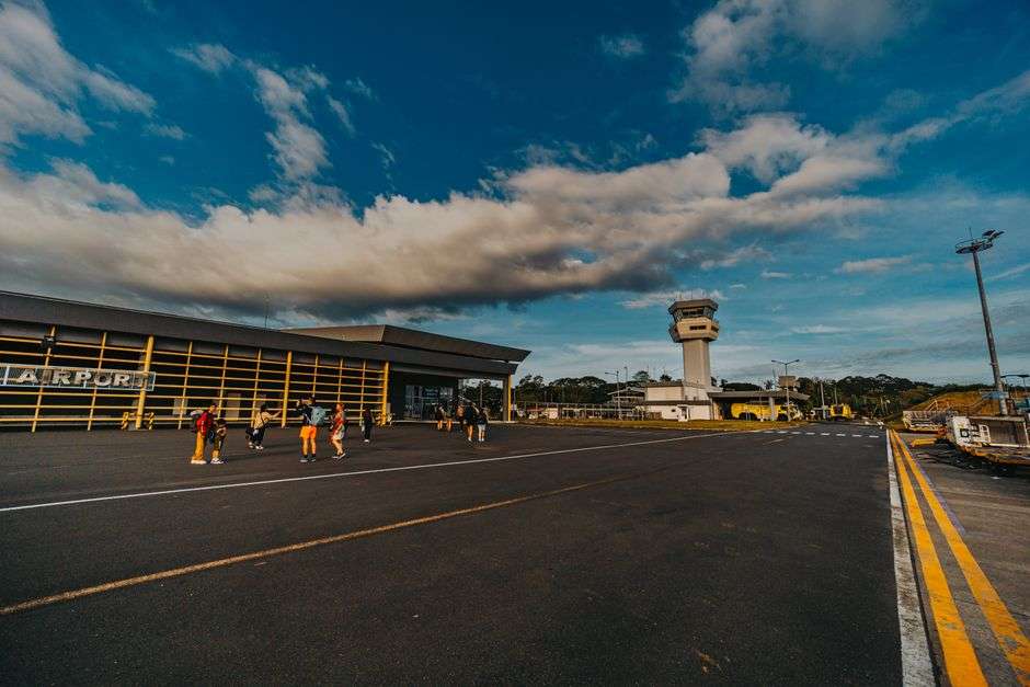 A small airport terminal building with travelers walking across the tarmac toward the gate