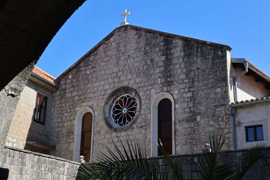 Stone facade of a Catholic church with a cross and arched windows