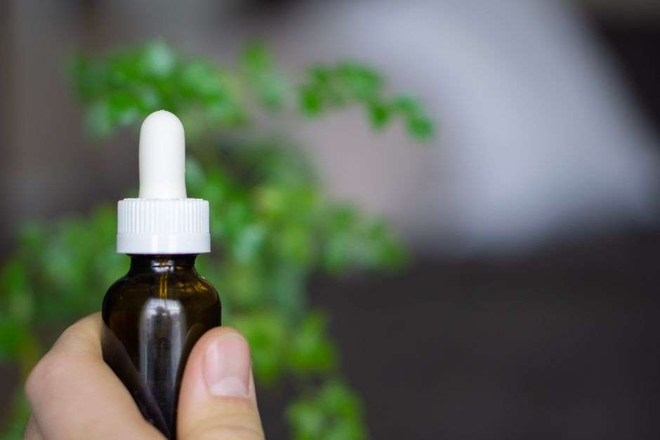 A hand holds a dropper bottle of CBD oil