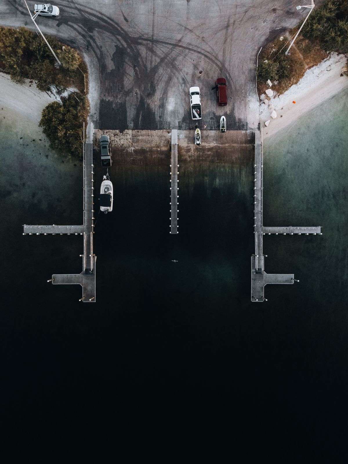 Aerial view of a two-lane boat ramp with finger piers and truck-trailer parking near the water