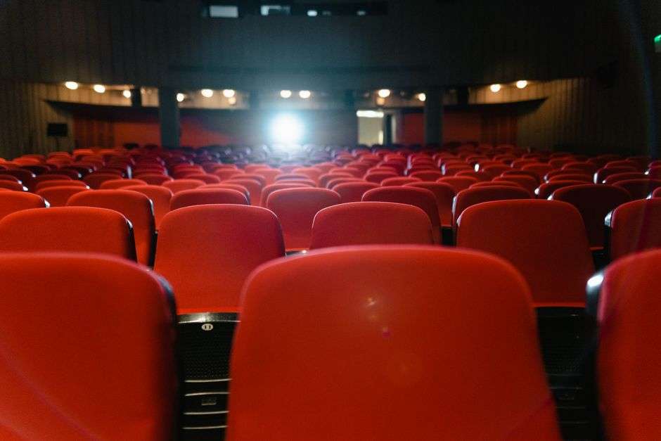 Empty movie theater with rows of red seats facing an illuminated screen