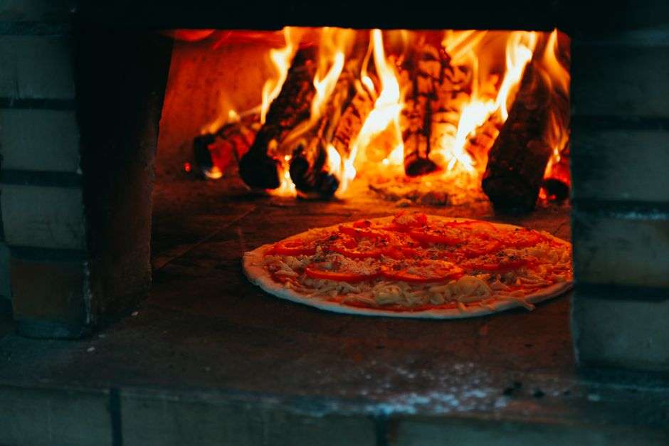 Pizza baking in a coal-fired brick oven with visible flames