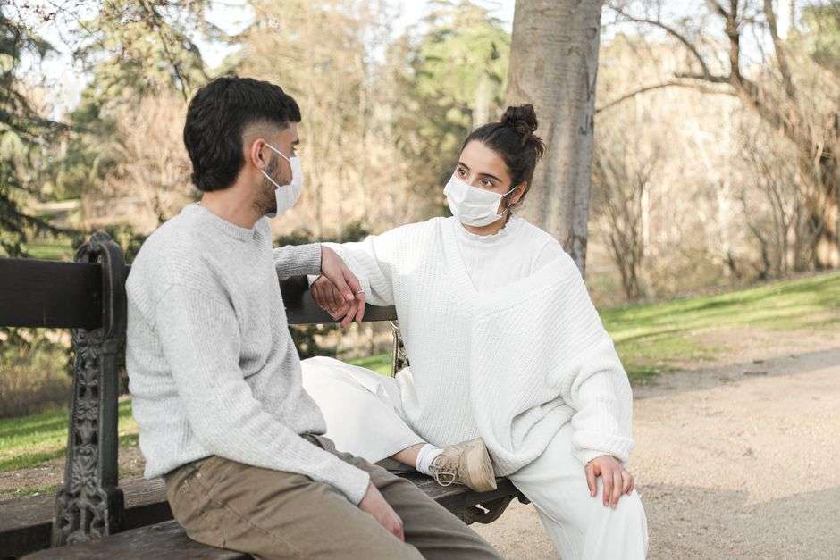 Two people sit at a distance from each other on a park bench, practicing physical distancing outdoors
