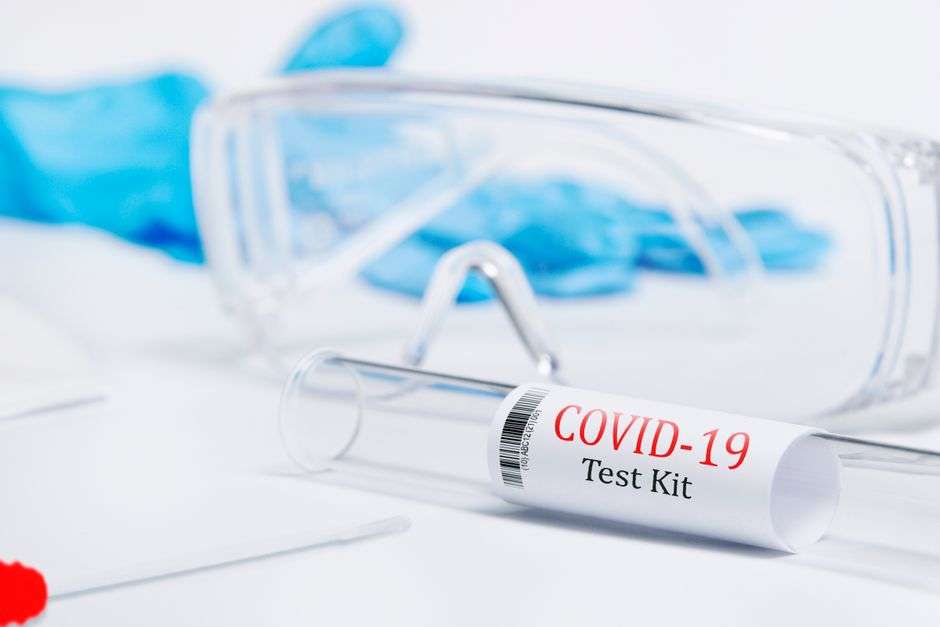 A COVID-19 test kit tube next to a pair of safety glasses on a lab surface