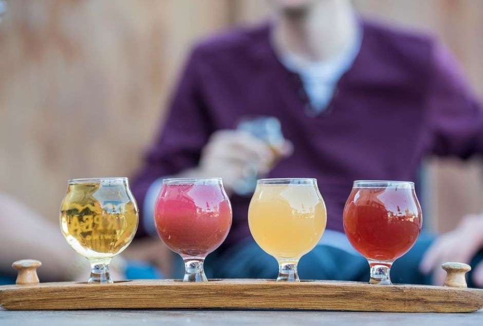 A flight of colorful craft beers in glasses lined up on a wooden serving board at a brewery taproom