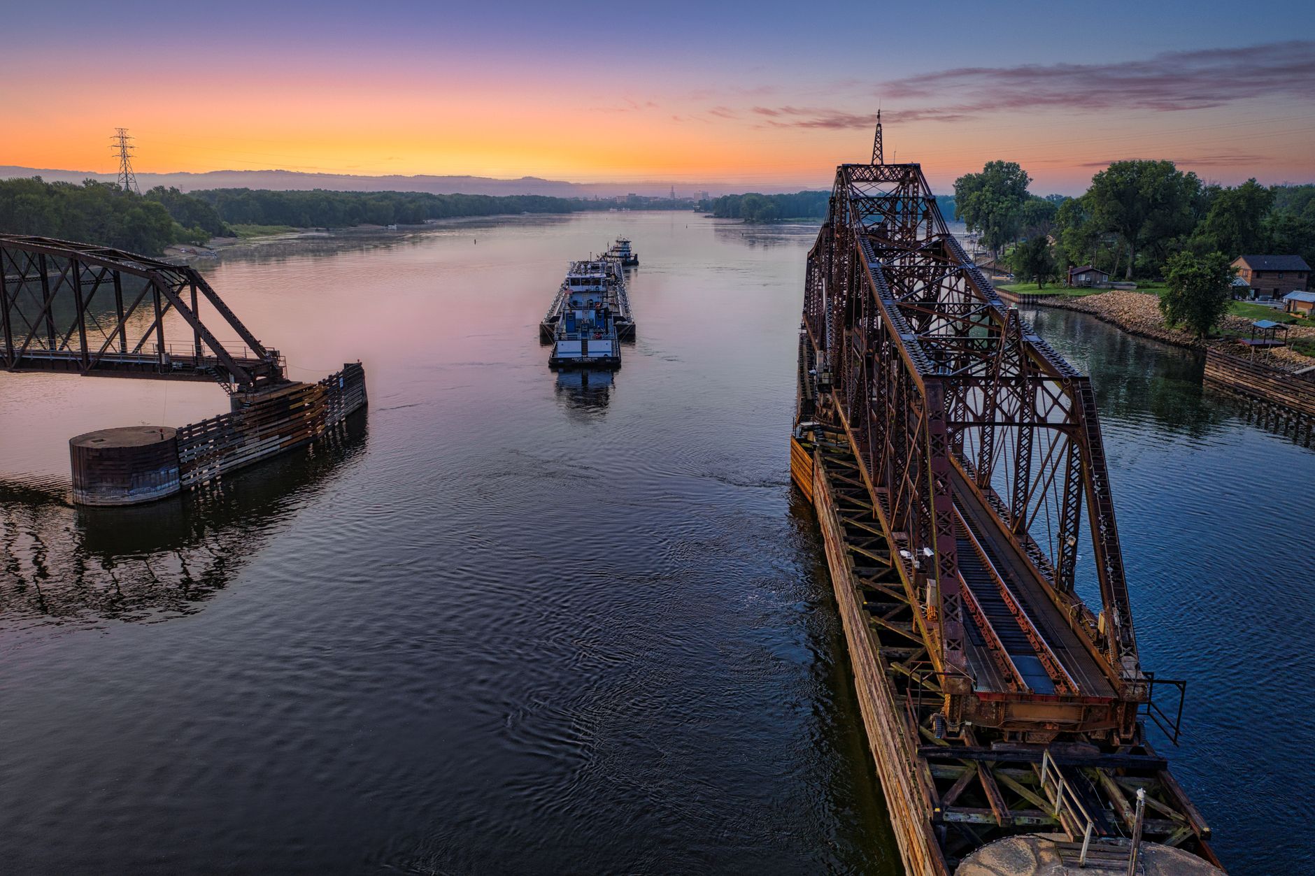 A low railroad bridge crossing a wide river used by barge traffic