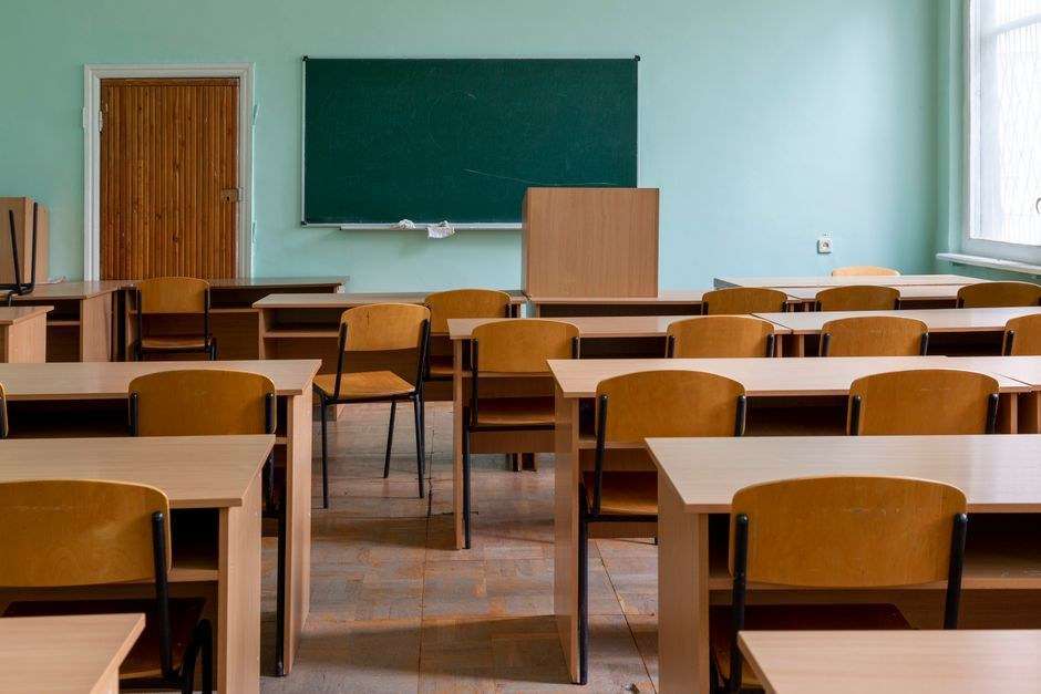 An empty classroom with wooden desks, chairs and a green chalkboard