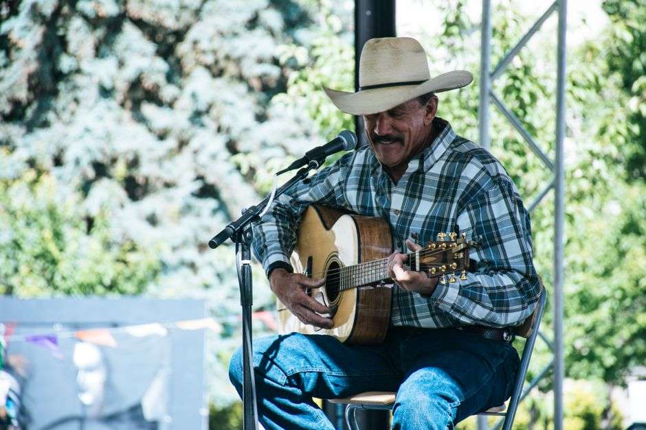 A musician wearing a cowboy hat performs on an acoustic guitar during an outdoor country music show
