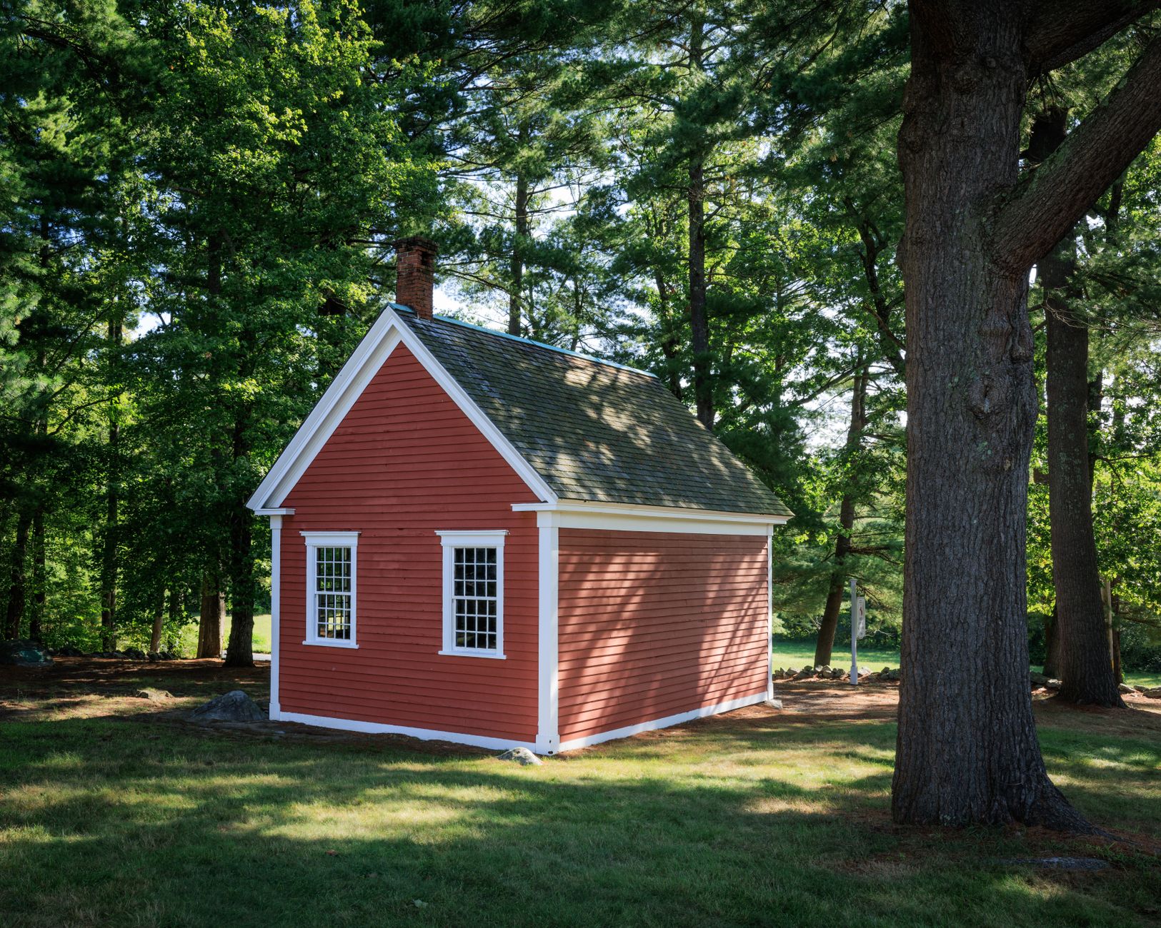 A small red historic schoolhouse building near the coast