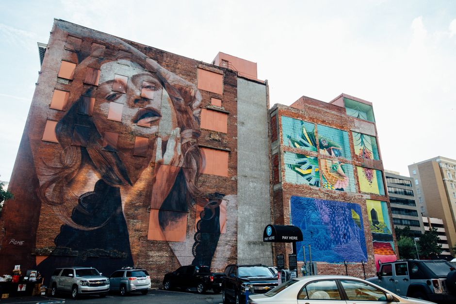 Volunteers painting a large colorful mural on a downtown building wall