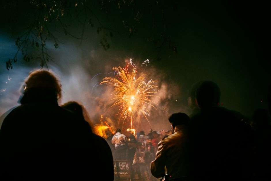 A large crowd gathers downtown at night to watch a New Year's Eve fireworks display