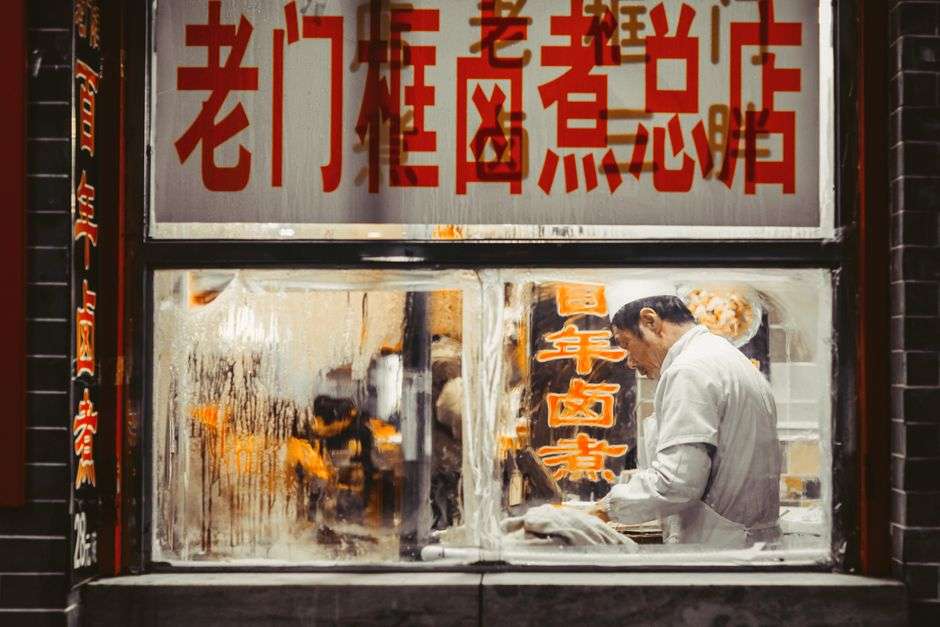 A cook works at a stainless steel counter in a busy restaurant kitchen