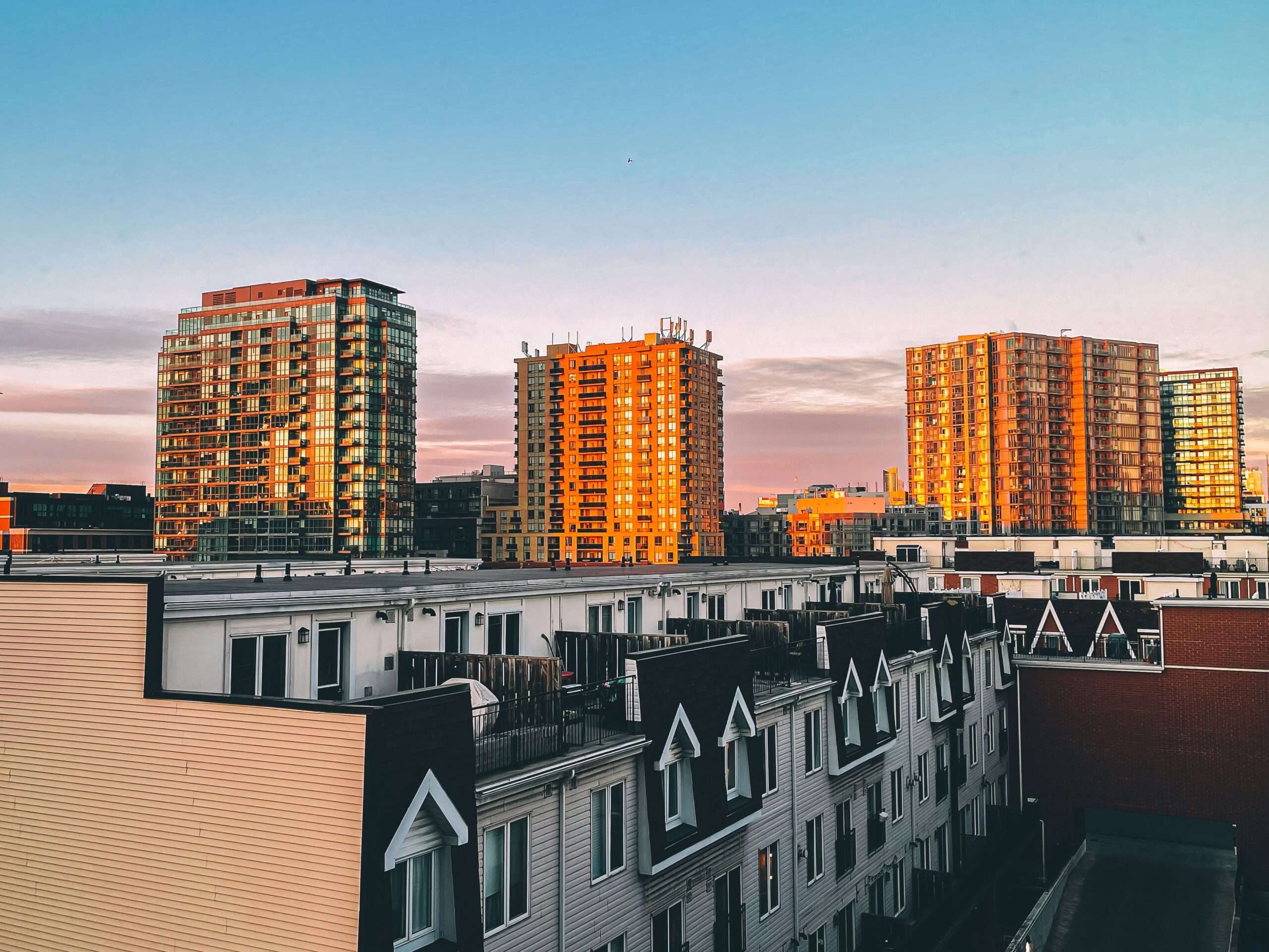 A modern city skyline featuring residential apartment buildings illuminated by morning sunrise