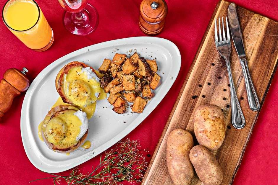 Plate of eggs Benedict served with hash browns and hollandaise sauce at a brunch restaurant