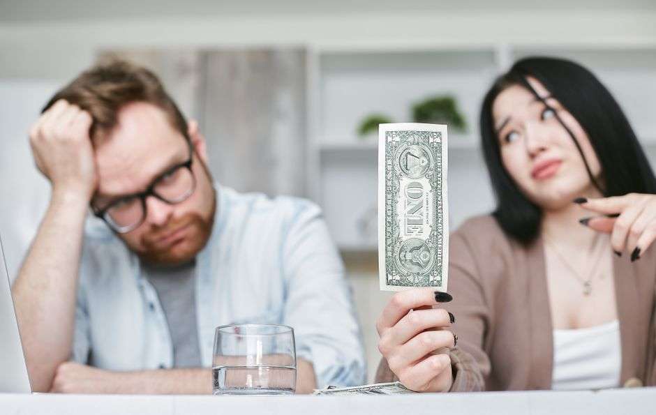 A parent sits at a kitchen table reviewing bills, reflecting the financial strain many households face despite living in an outwardly prosperous community.