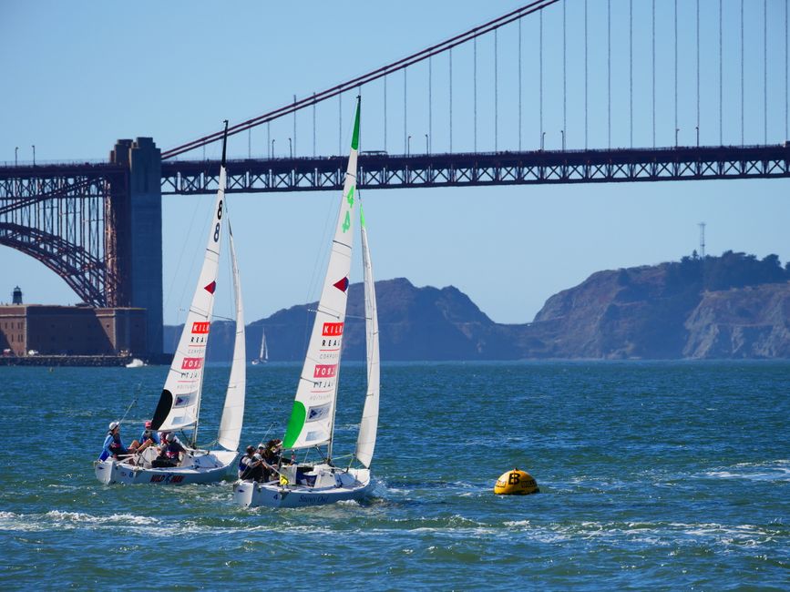 A sailboat competing on open water near a coastal community