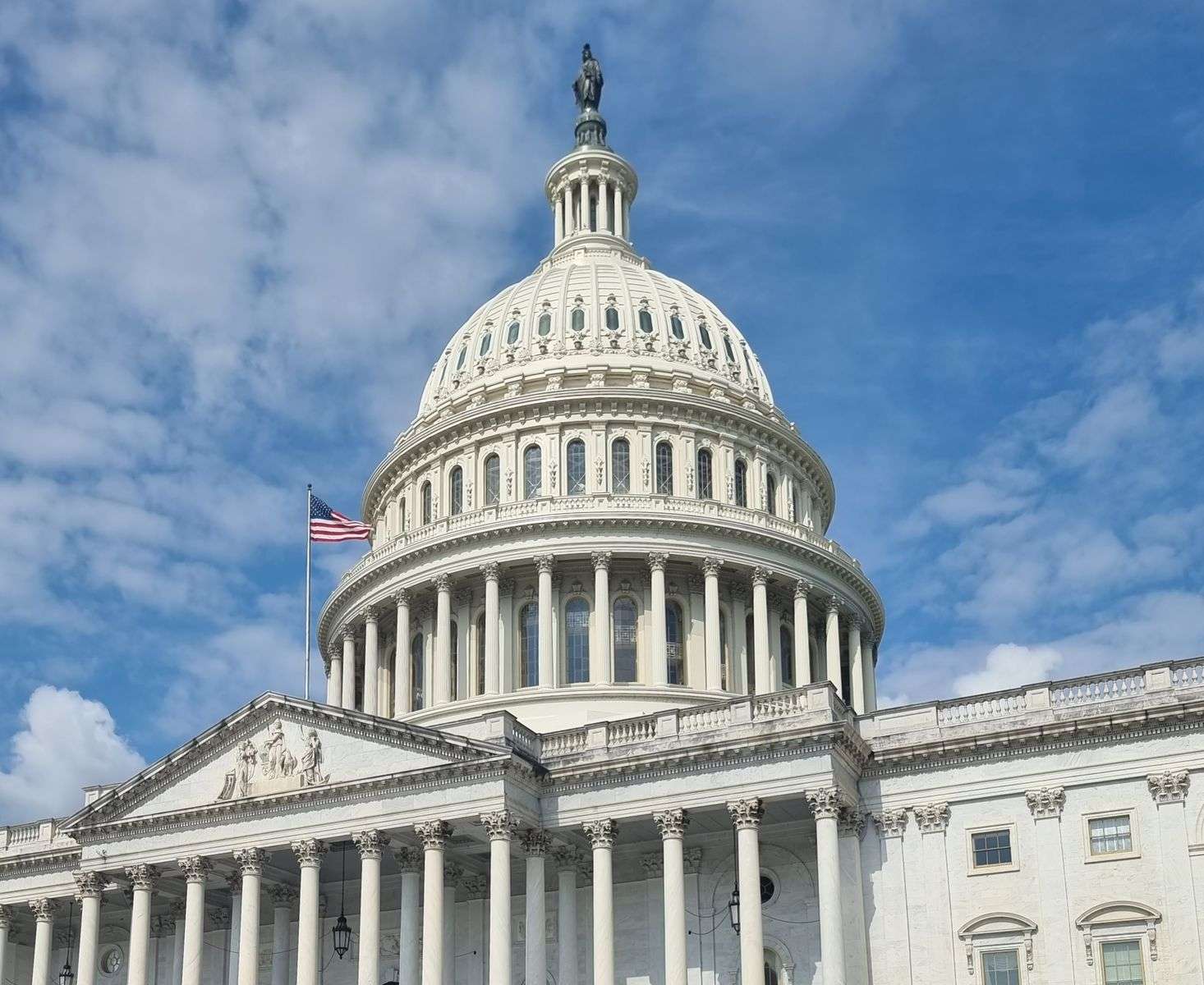 The U.S. Capitol dome with an American flag against a clear blue sky