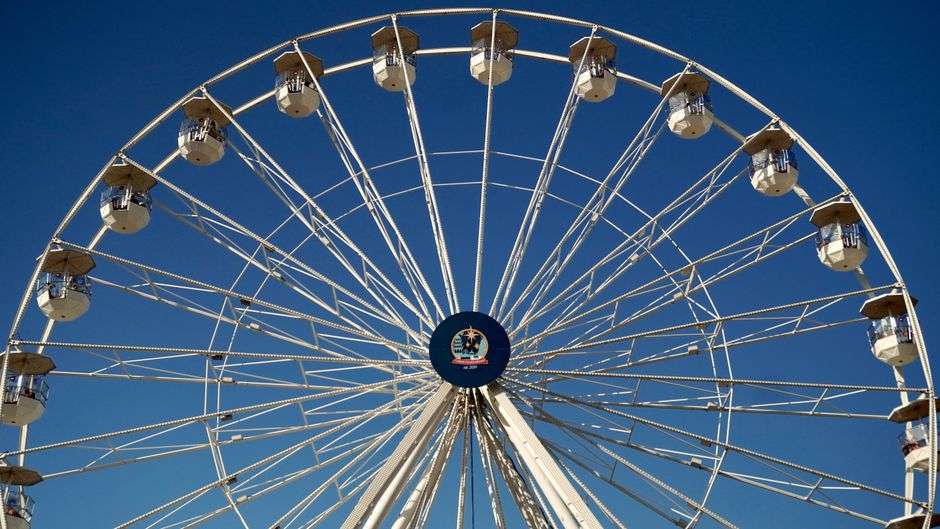 A brightly lit Ferris wheel towers over a county fair midway under a clear sky