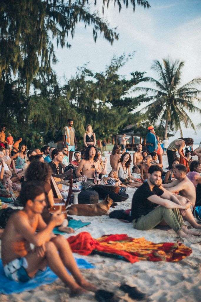 Large crowd gathered on a Gulf Coast beach for an outdoor music festival at sunset