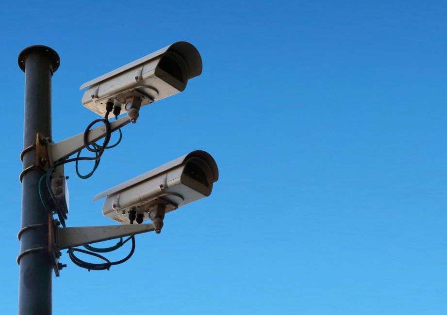 A security camera mounted on a pole against a clear blue sky near the beach