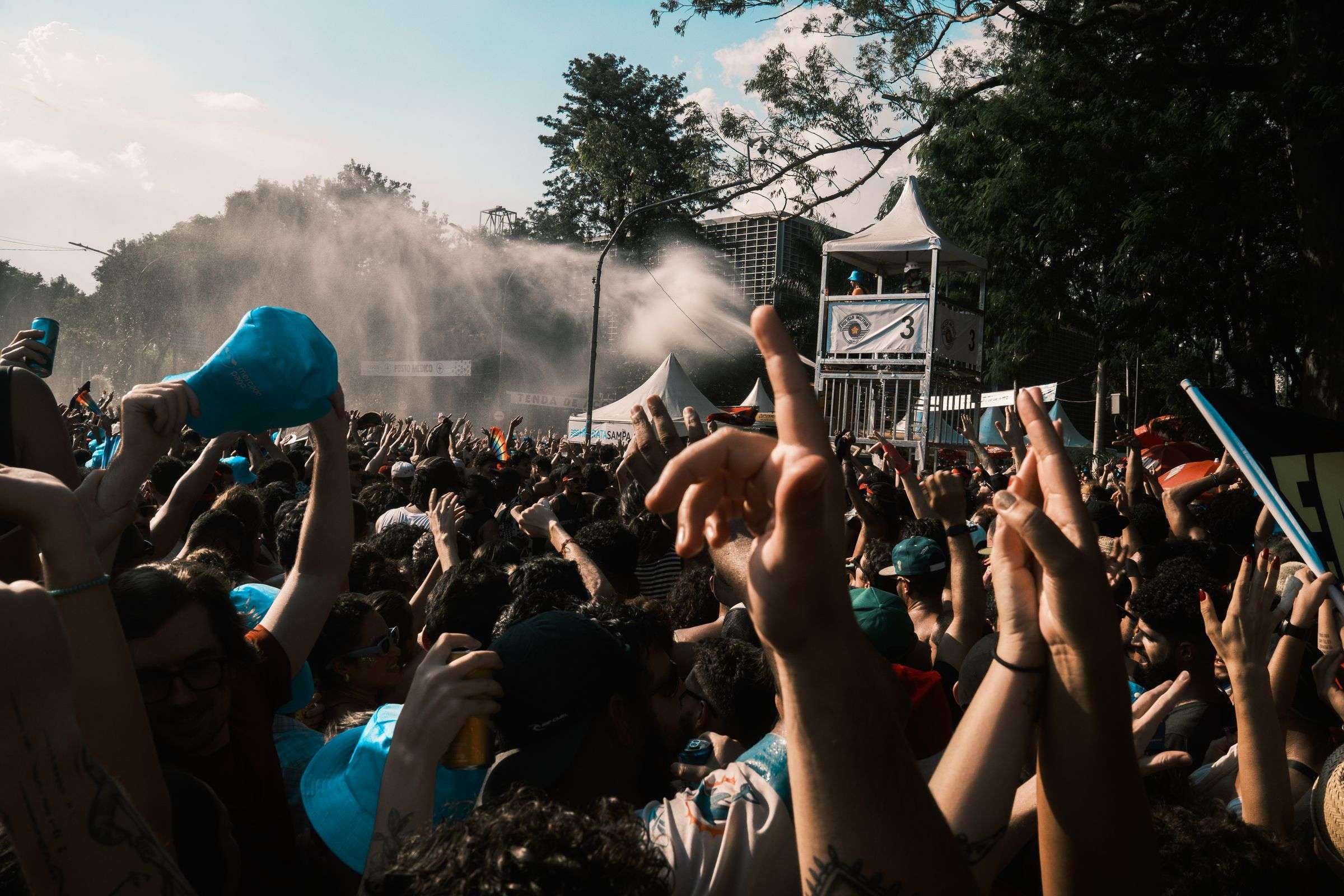 A large crowd gathers outdoors for a music festival on a sunny day