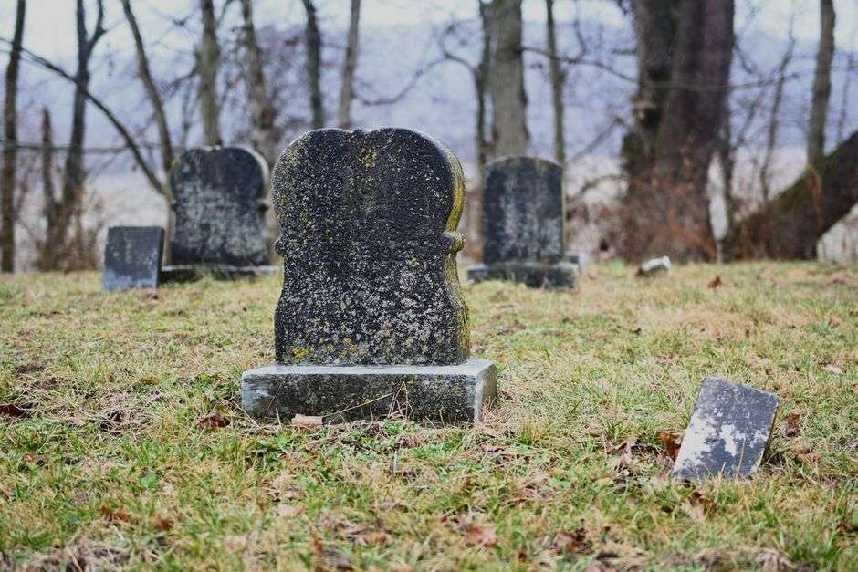 Weathered, moss-covered headstones stand beneath tall trees in an old Mobile-area cemetery.