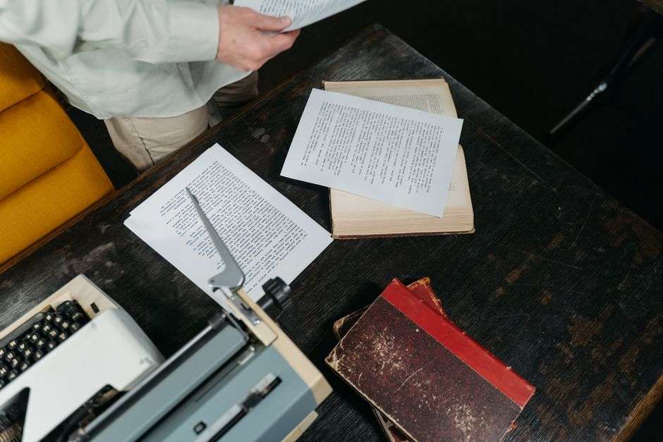 Vintage typewriter surrounded by stacks of books and papers on a wooden desk