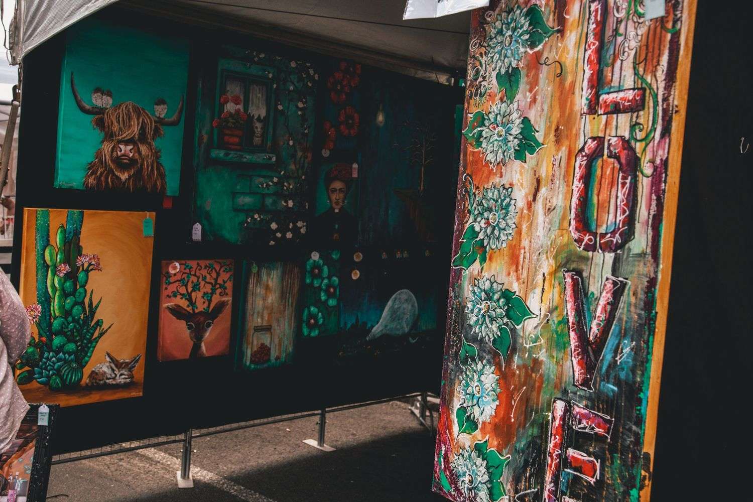 Colorful paintings and handmade artwork displayed at an outdoor art festival vendor booth