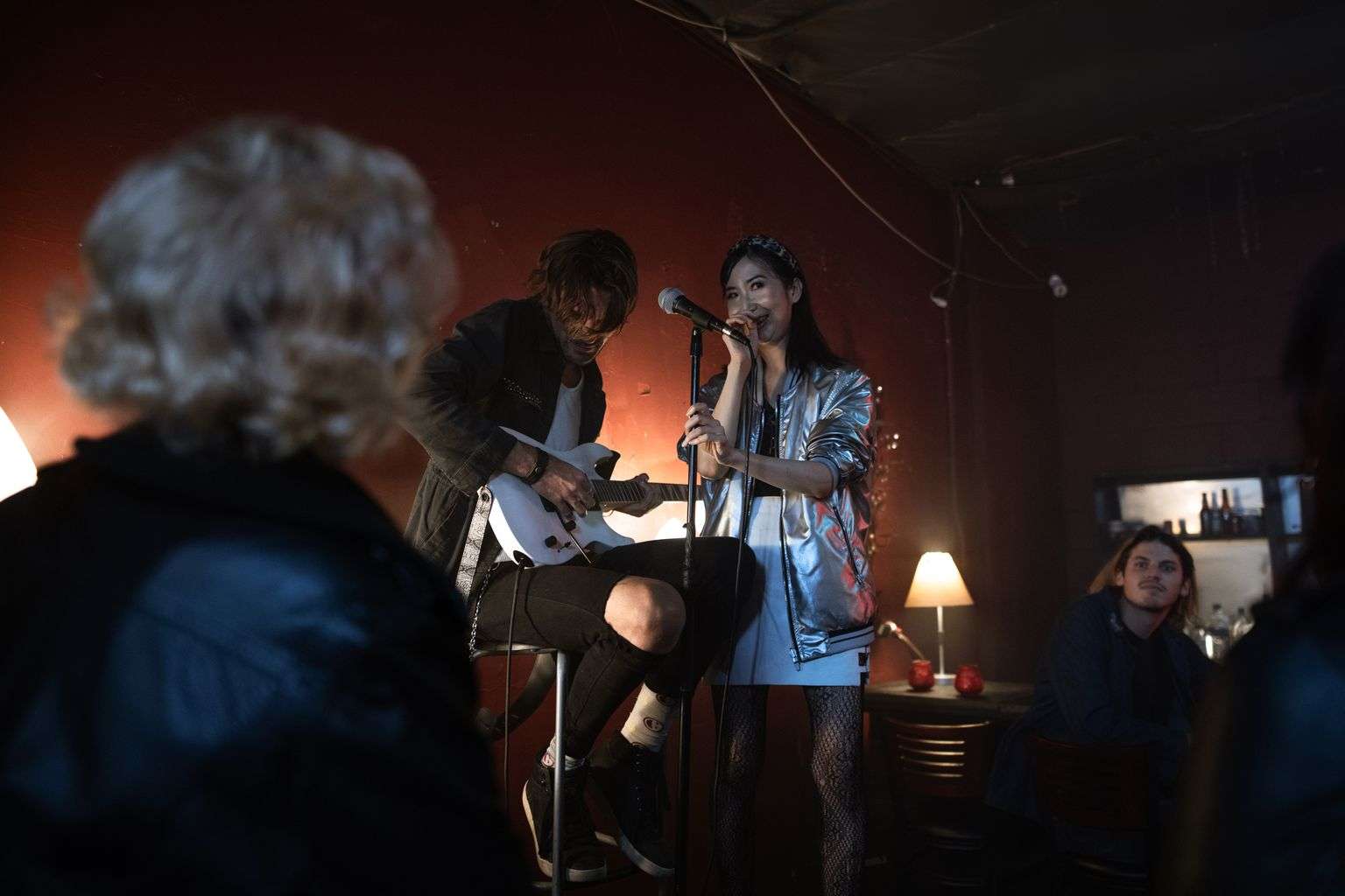 A guitarist and vocalist perform an acoustic duet in a dimly lit, intimate bar setting