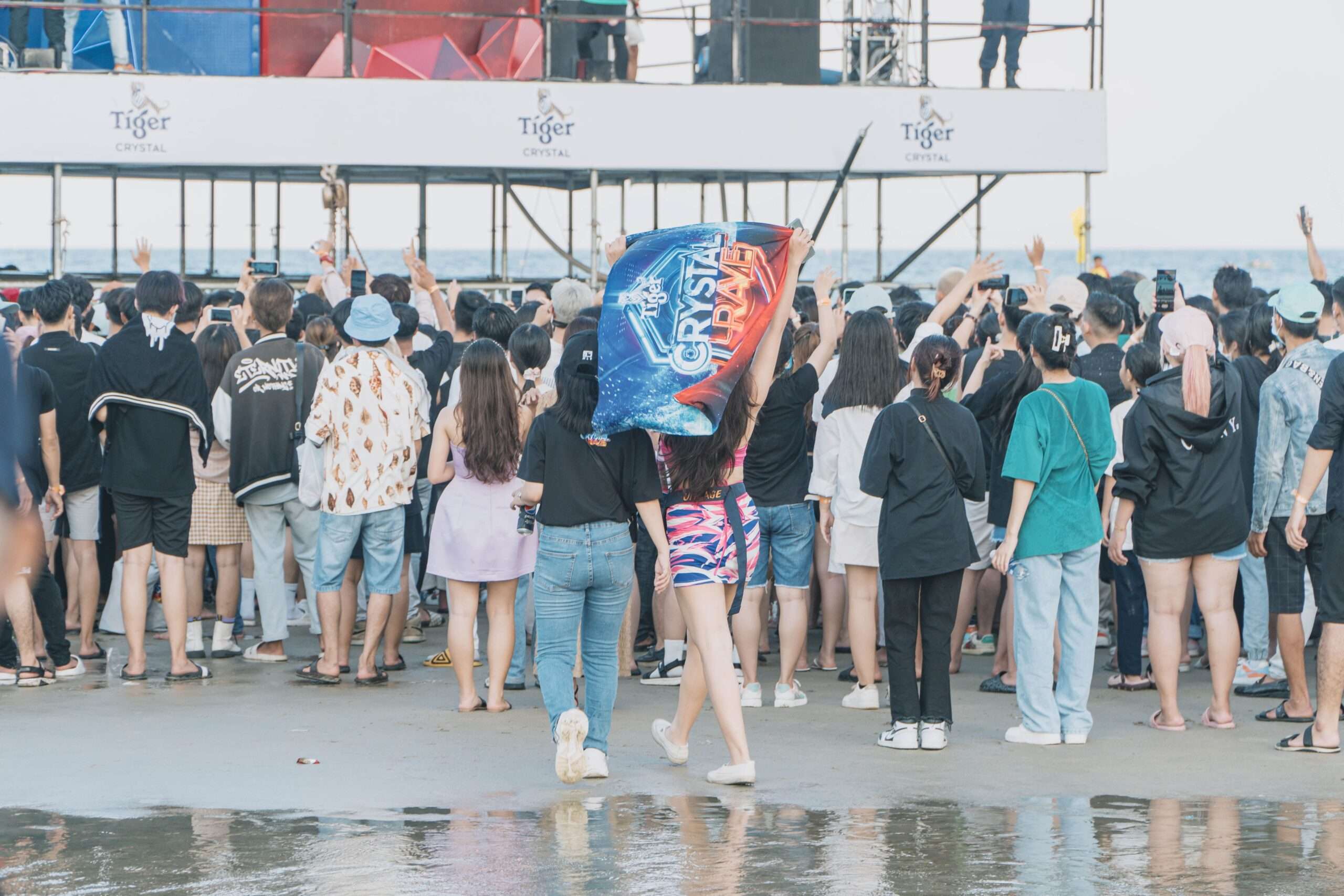 Large crowd gathered on a beach enjoying an outdoor music festival at sunset