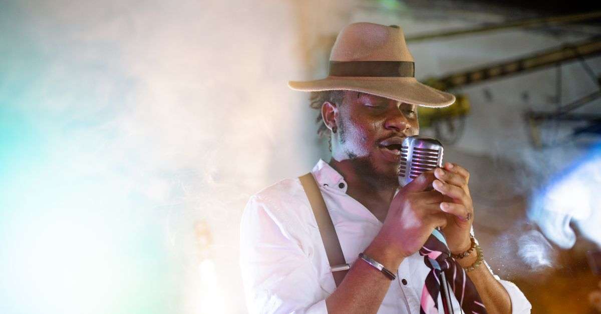 A vintage-style singer in a hat performs into a microphone under stage lights