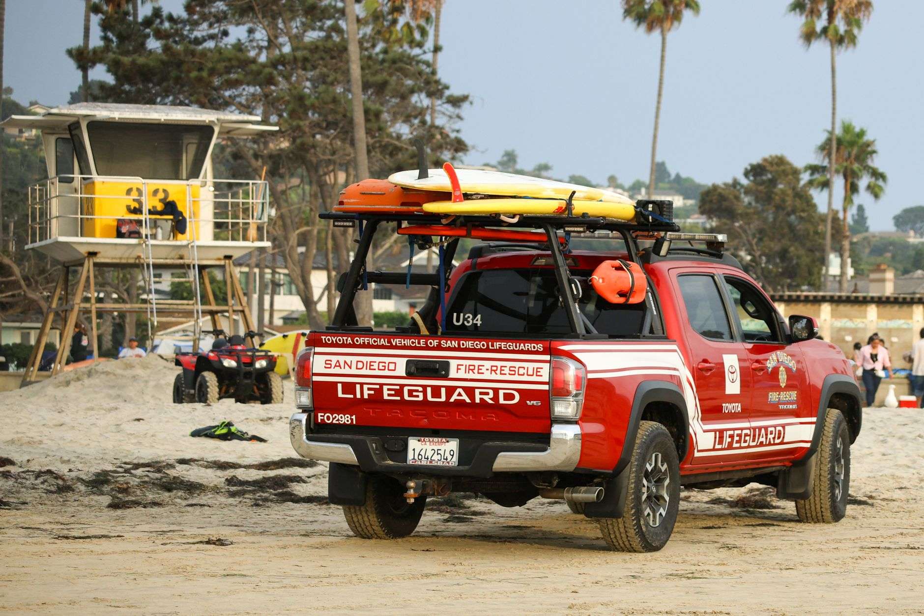 A lifeguard truck parked on a sandy beach near a lifeguard tower