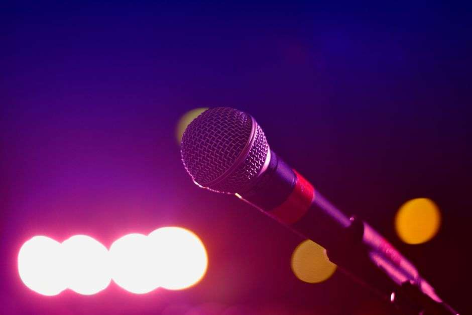 A microphone glows under colorful stage lighting inside a bar, evoking a karaoke night at a local sports bar.