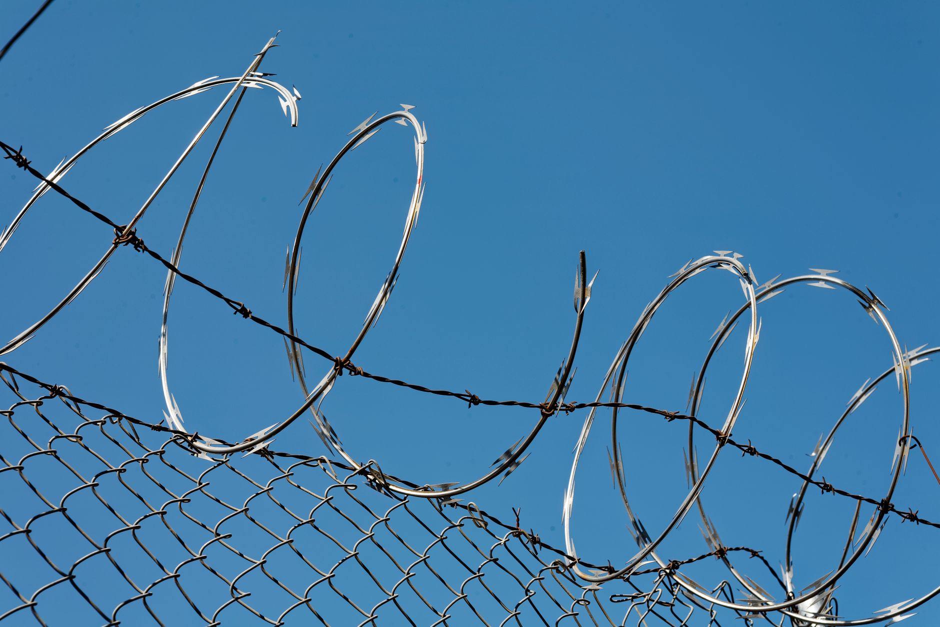 A prison perimeter fence topped with razor wire against an overcast sky