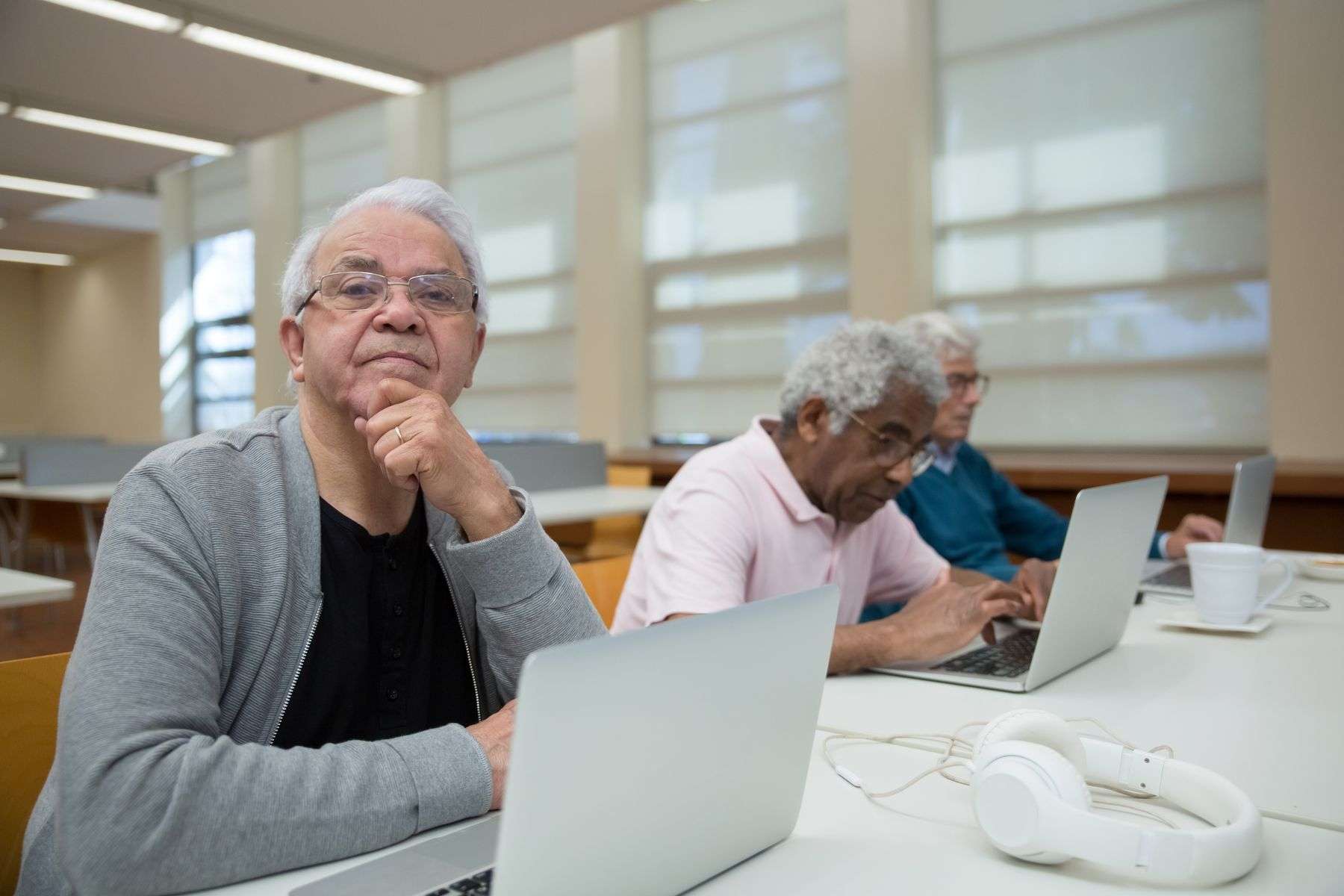 An older adult sitting at a table learning to use a laptop computer