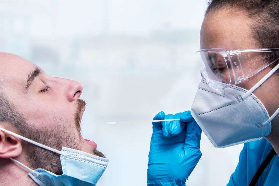 A healthcare worker in protective gear administers a nasal swab COVID-19 test to a patient at a testing site.